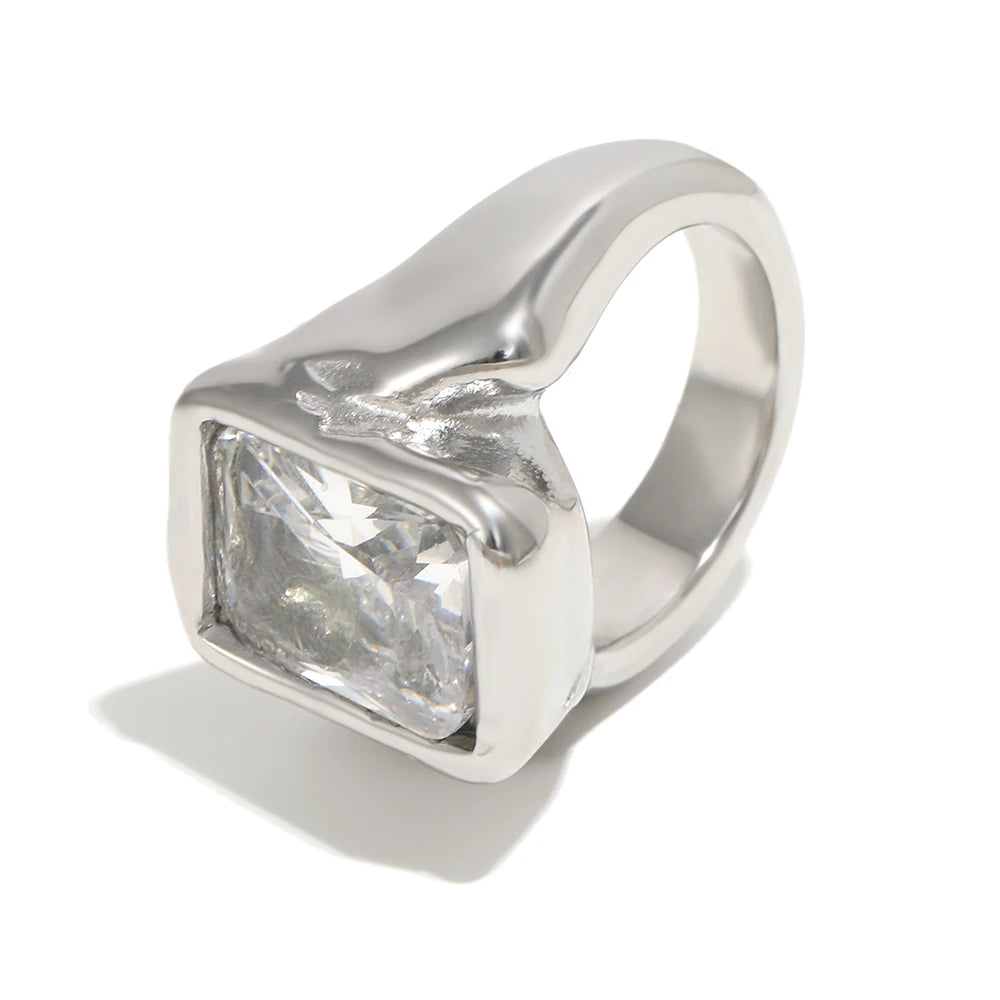 Silver oversized emerald cut chunky ring on white background, large clear faceted rectangular stone inside organic-profile silver bezel, wide chunky band with irregular shoulder outline, cool light, long cool shadow
