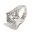 Silver oversized emerald cut chunky ring on white background, large clear faceted rectangular stone inside organic-profile silver bezel, wide chunky band with irregular shoulder outline, cool light, long cool shadow
