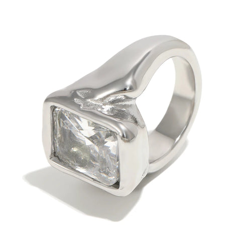 Silver oversized emerald cut chunky ring on white background, large clear faceted rectangular stone inside organic-profile silver bezel, wide chunky band with irregular shoulder outline, cool light, long cool shadow
