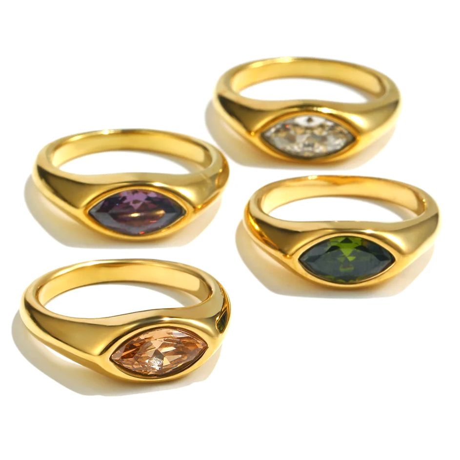 Four gold marquise stone dome signet rings on white background showing all four colorways, brown amber, purple, white crystal, and green stones bezel-set in mirror-polished dome bands
