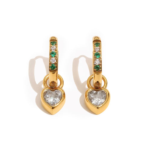 Gold huggie hoop earrings with alternating green and white pavé stones and bezel-set heart charm drop on white background, warm directional shadow
