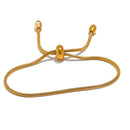 Gold snake chain slider bracelet on white background, oval loop shape with barrel slider at center, two snake chain ends with oval tips, warm light with soft directional shadow beneath

