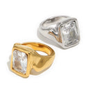 Gold and silver oversized emerald cut chunky rings on white background, large clear faceted rectangular stone set in organic-profile wide band, both colorways shown together with soft warm shadow
