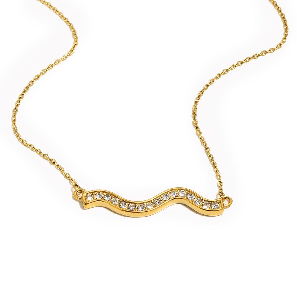 Gold pavé wave bar necklace on white background, S-curve wave pendant fully set with rhinestones edge to edge, fine O-chain, warm soft shadow beneath pendant
