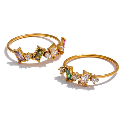 Two gold geometric multi-stone rings on white background, upper ring with purple, olive green and clear baguette stones with round accents, lower ring with deep green and clear baguette stones, fine gold bands, warm light with long shadows
