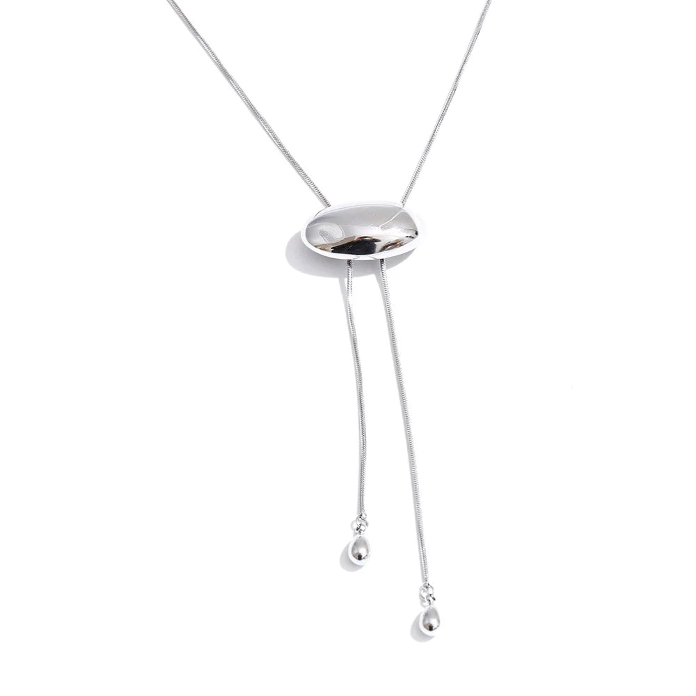 Silver oval slider lariat necklace on white background, polished dome oval slider on fine snake chain, two ends hanging at uneven lengths with teardrop tips, cool light with soft shadow beneath oval
