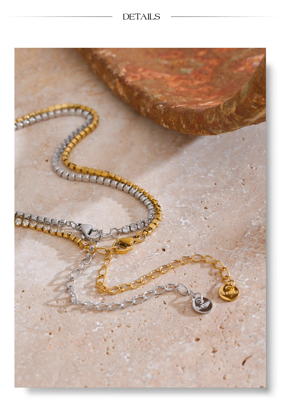 Gold and silver round stone tennis necklaces laid side by side on cream stone surface, both colorways showing continuous prong-set stones with lobster clasps, extender chains and engraved round tags, terracotta stone in background
