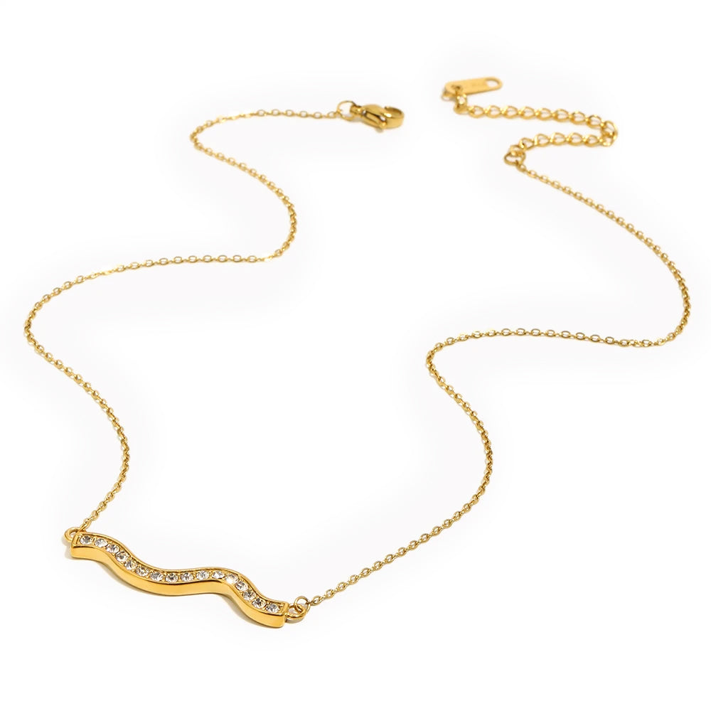 Gold pavé wave bar necklace on light grey-white background, overhead angled view showing full chain length with lobster clasp and extender at top, rhinestone wave pendant at bottom, fine O-chain links visible
