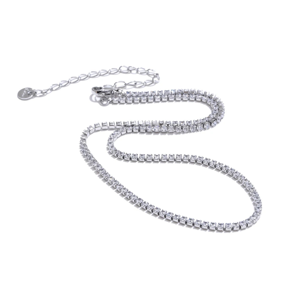 Silver round stone tennis necklace on white background, continuous prong-set round stones along full length, lobster clasp with extender chain and round tag pendant, cool light with soft shadow
