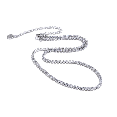 Silver round stone tennis necklace on white background, continuous prong-set round stones along full length, lobster clasp with extender chain and round tag pendant, cool light with soft shadow
